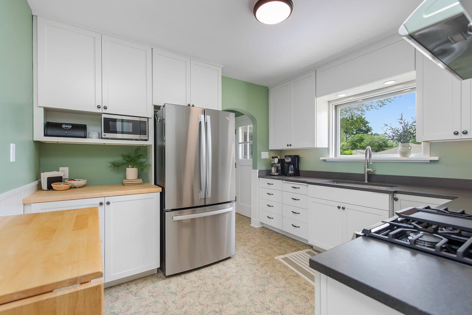 Remodeled kitchen with white shaker cabinets, sage-green walls, and butcher-block counters